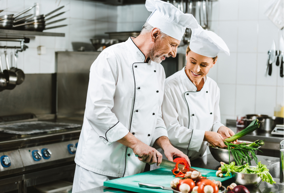 chefs féminins et masculins souriants en uniforme et chapeaux cuisinant dans la cuisine du restaurant