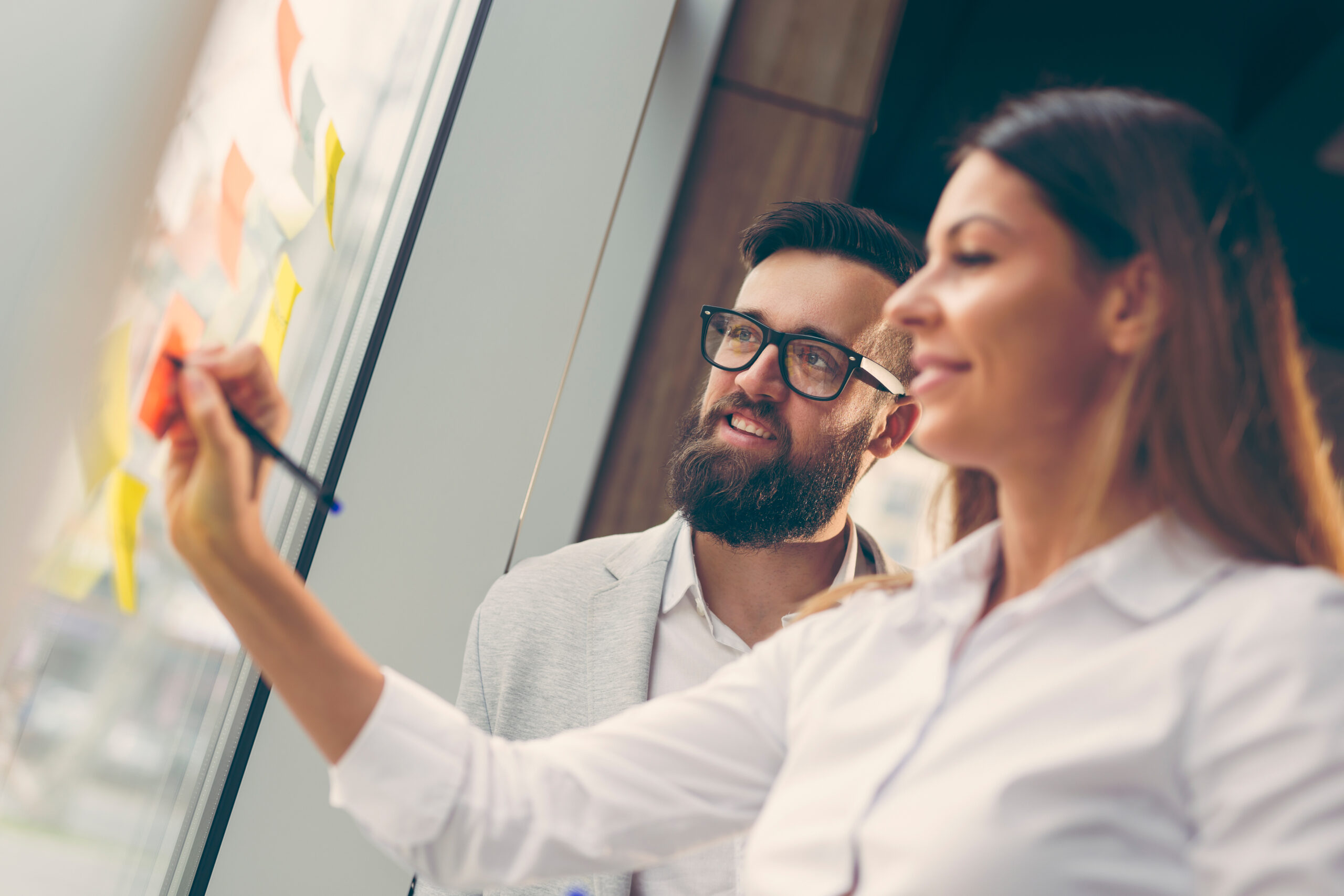 Homme d'affaires et femme d'affaires faisant un remue-méninges à l'aide de notes autocollantes sur un mur de verre dans un bureau